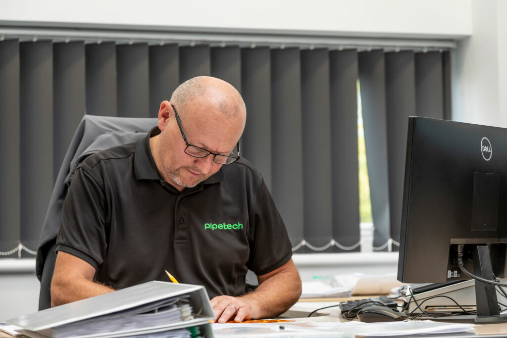 A man sat at an office desk wearing a black branded t-shirt.
