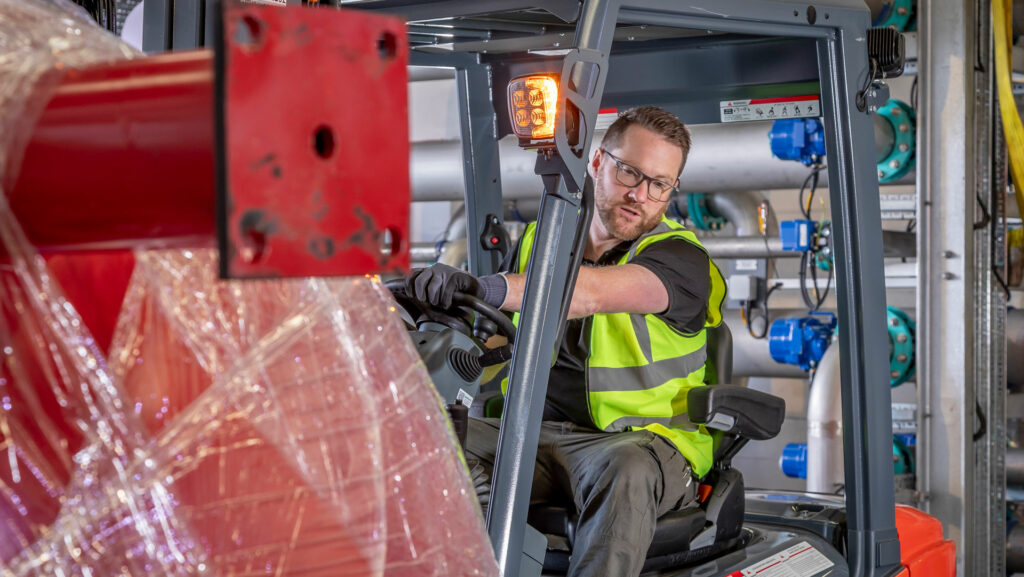A man wearing a high-vis vest driving a forklift truck in a workshop