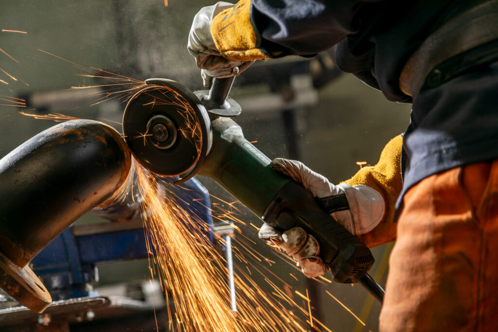 Fabricator using an angle grinder on a metal pipe, producing sparks.