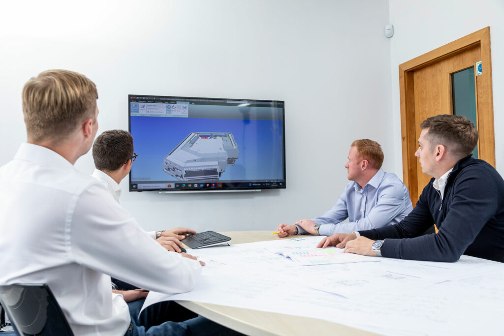 Four men sat around a table in an office, looking at a technical drawing on an interactive screen.