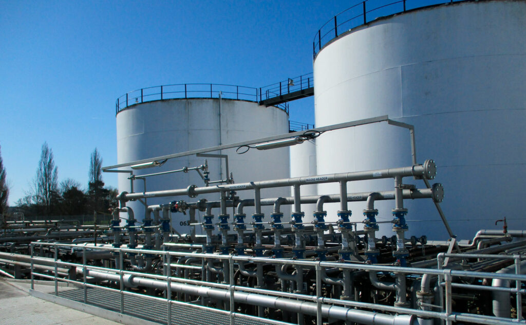 Industrial plant with large white storage tanks and an array of interconnecting pipelines.