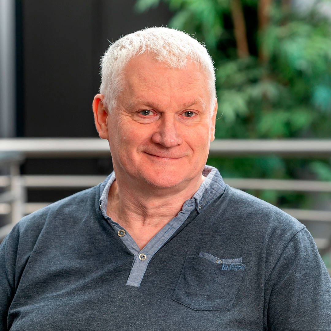 Man with white hair wearing a navy blue tshirt.
