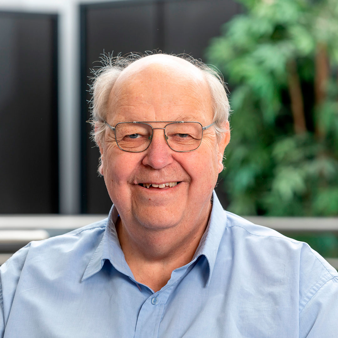 Man with grey hair and glasses, wearing a blue shirt.