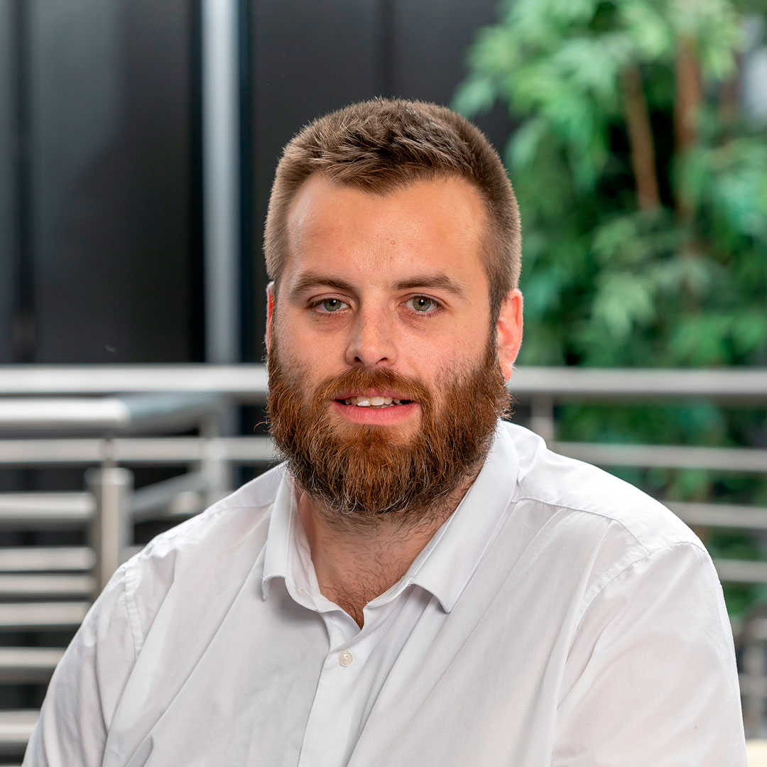Man with brown hair and a beard wearing a white shirt.