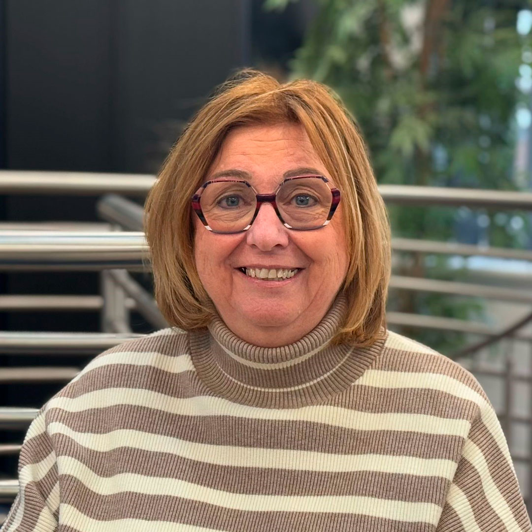 Lady with brown hair, wearing glasses and a brown and white striped roll neck top.