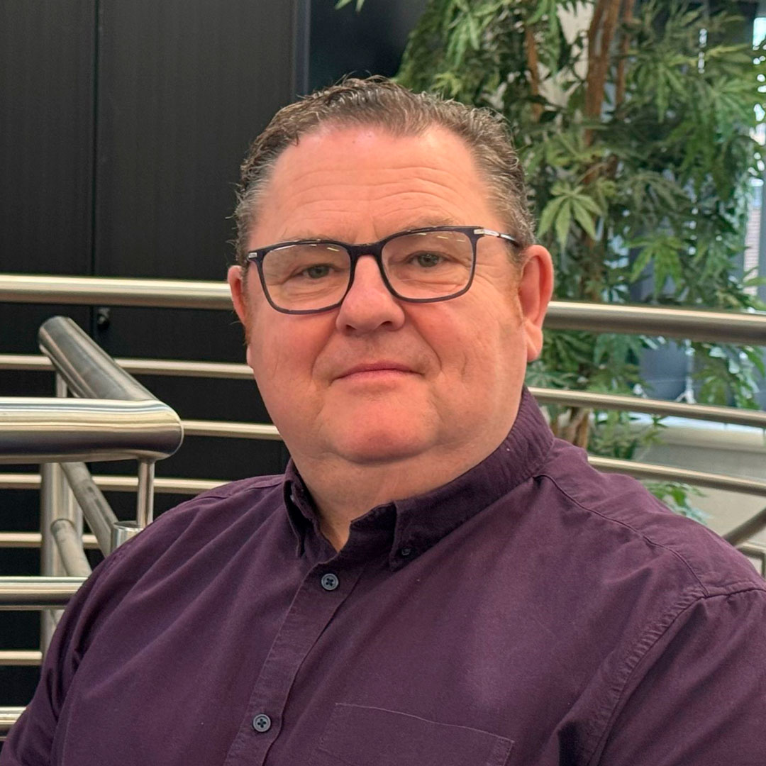 Man with brown hair and glasses, wearing a purple shirt.