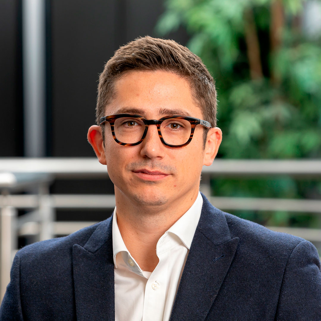 Man with brown hair, wearing glasses, a white shirt and a navy blazer.